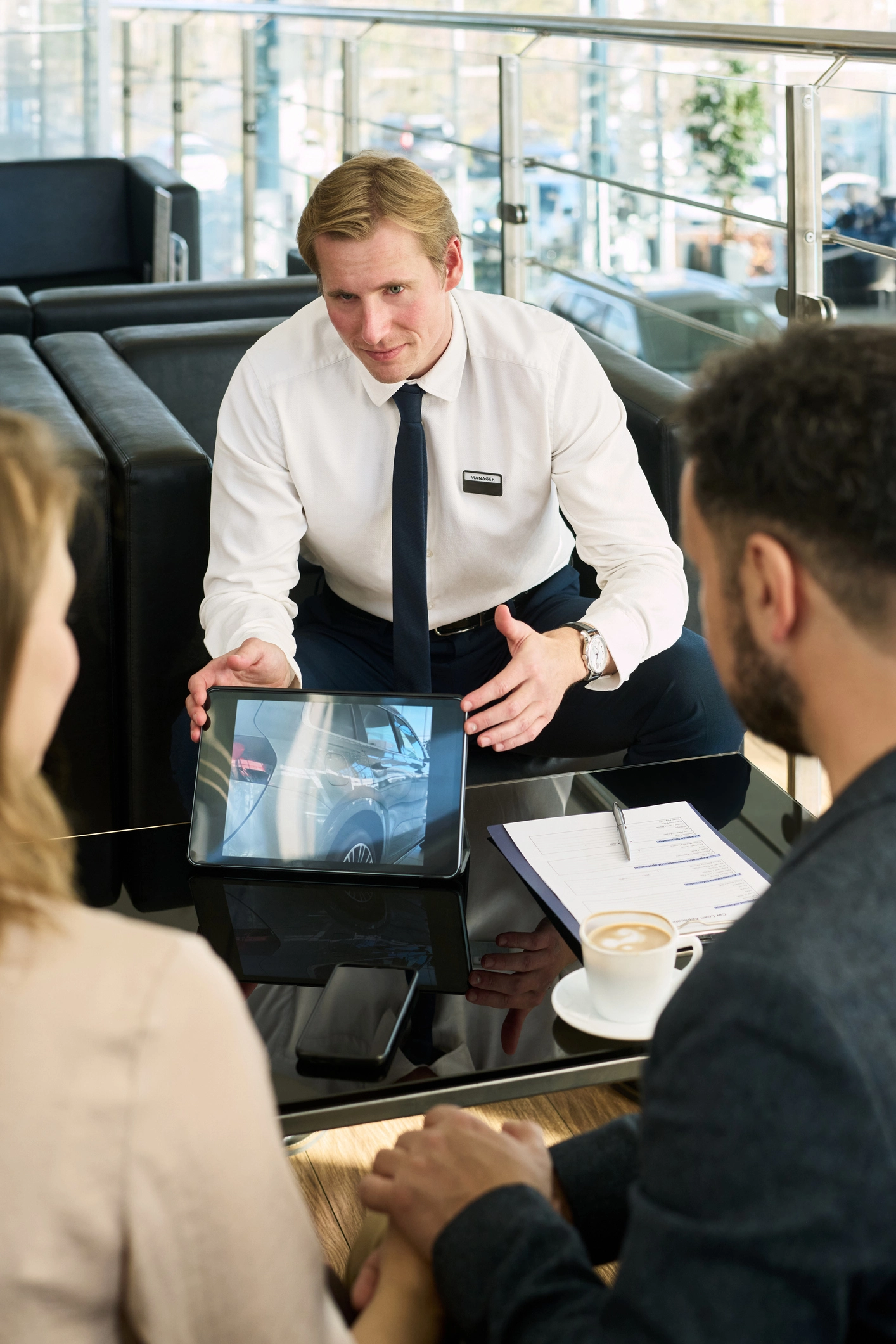 Mitarbeiter präsentiert zwei Kunden im Beratungsgespräch in einem Autohaus digitale Produktinformationen auf einem Tablet.